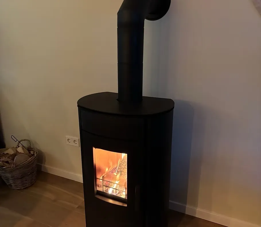 Zwarte houtkachel met rookkanaal en een mand haardhout in een woonkamer